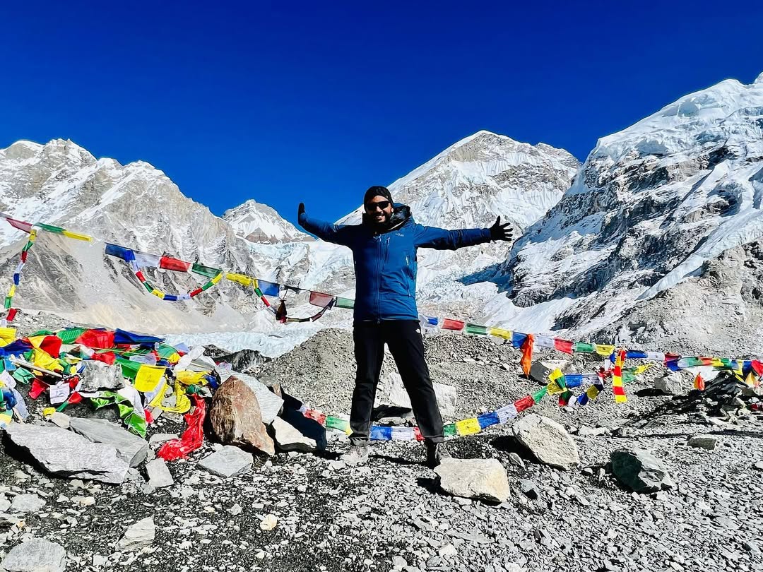 Charith De Silva with arms outstretched among prayer flags at Everest Base Camp